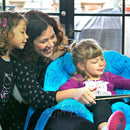 Mom and sisters reading a book, sitting snugly in the P Pod Postural Support System by Inspired by Drive.