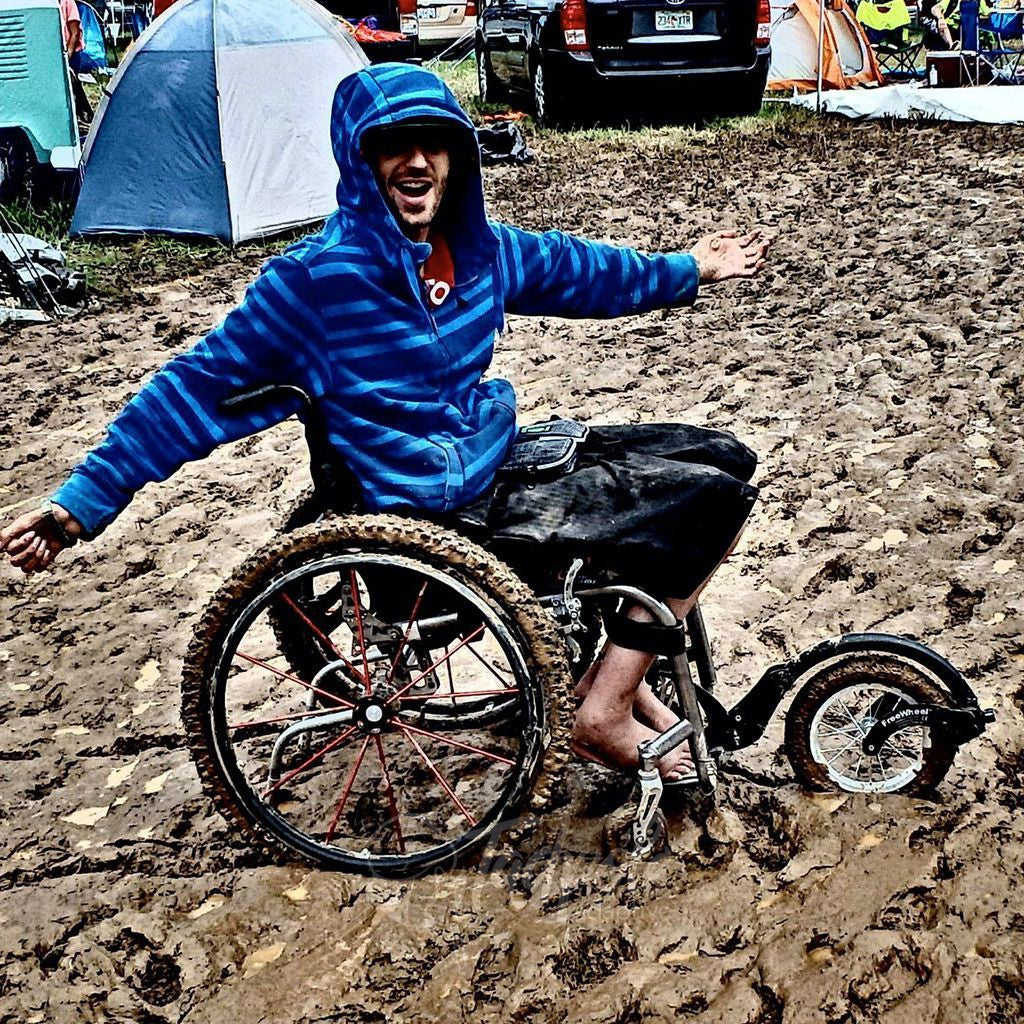Young man, deep in the mud, but mobile in his FreeWheel Wheelchair Attachment.
