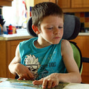 Boy in the kitchen, reading a book unattended in his Leckey Everyday Activity Seat.